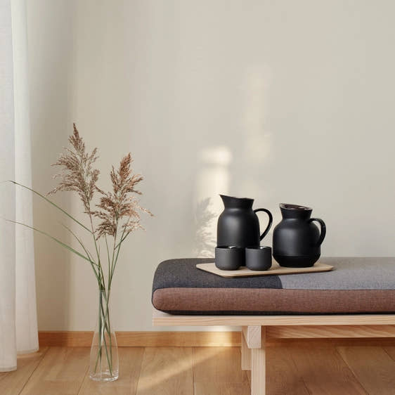 Two Stelton Amphora Vacuum Tea Jug in black on a bench table with two mugs and a plant in the background
