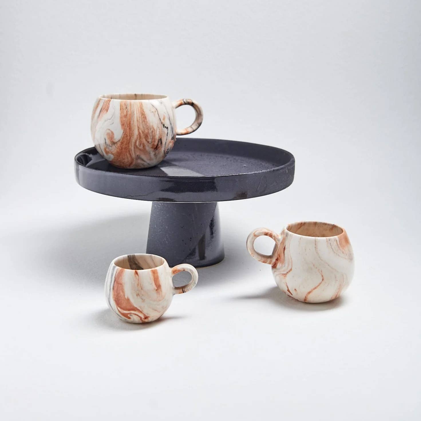 Egg Back Home Marble Mug Collection of 3 mugs in small, medium, and large displayed on and around a black pastry stand