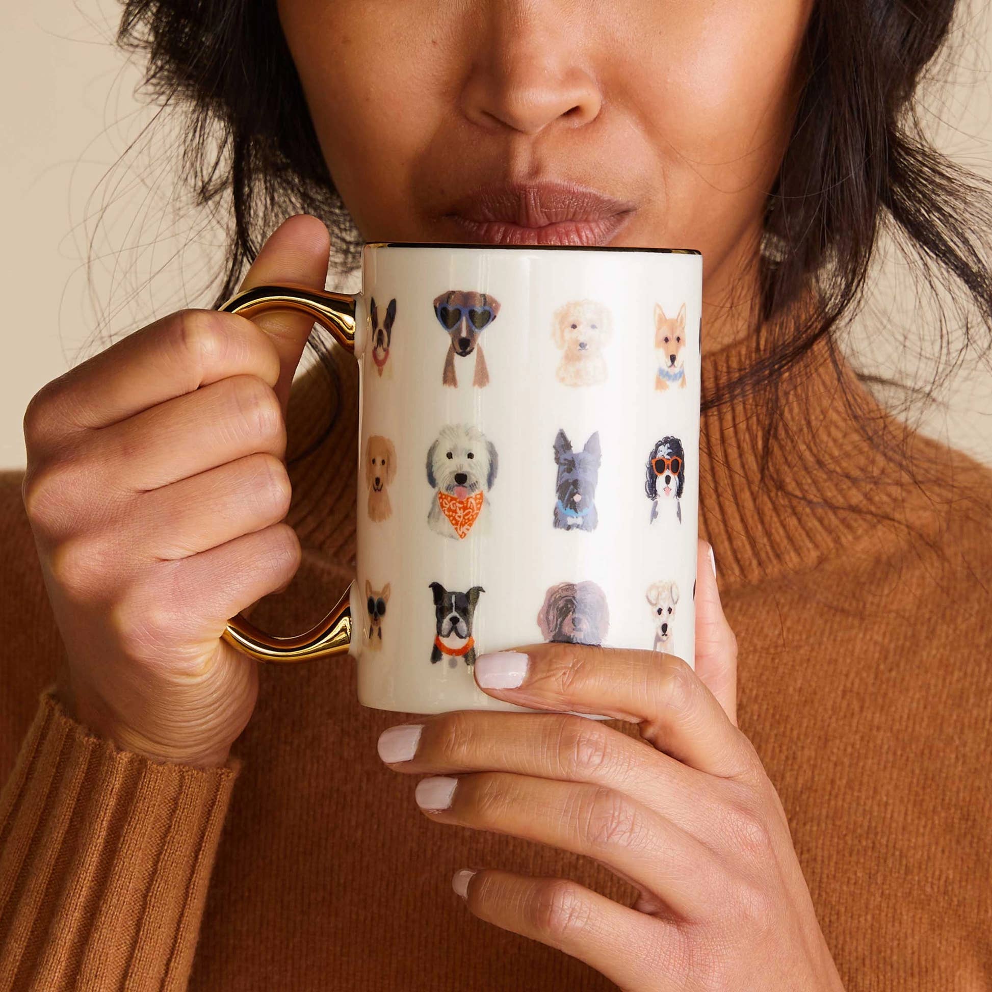 A person in a brown sweater holding and sipping tea from the Dogs Porcelain Mug by Rifle Paper Co 