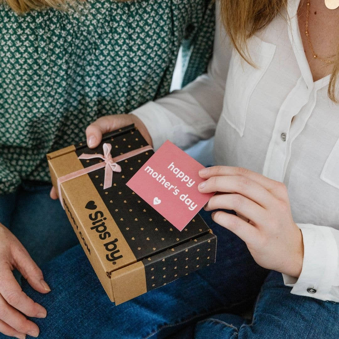 Person giving a mom a Sips by Box with a pink bow as a mother's day tea gift and happy mother's day postcard