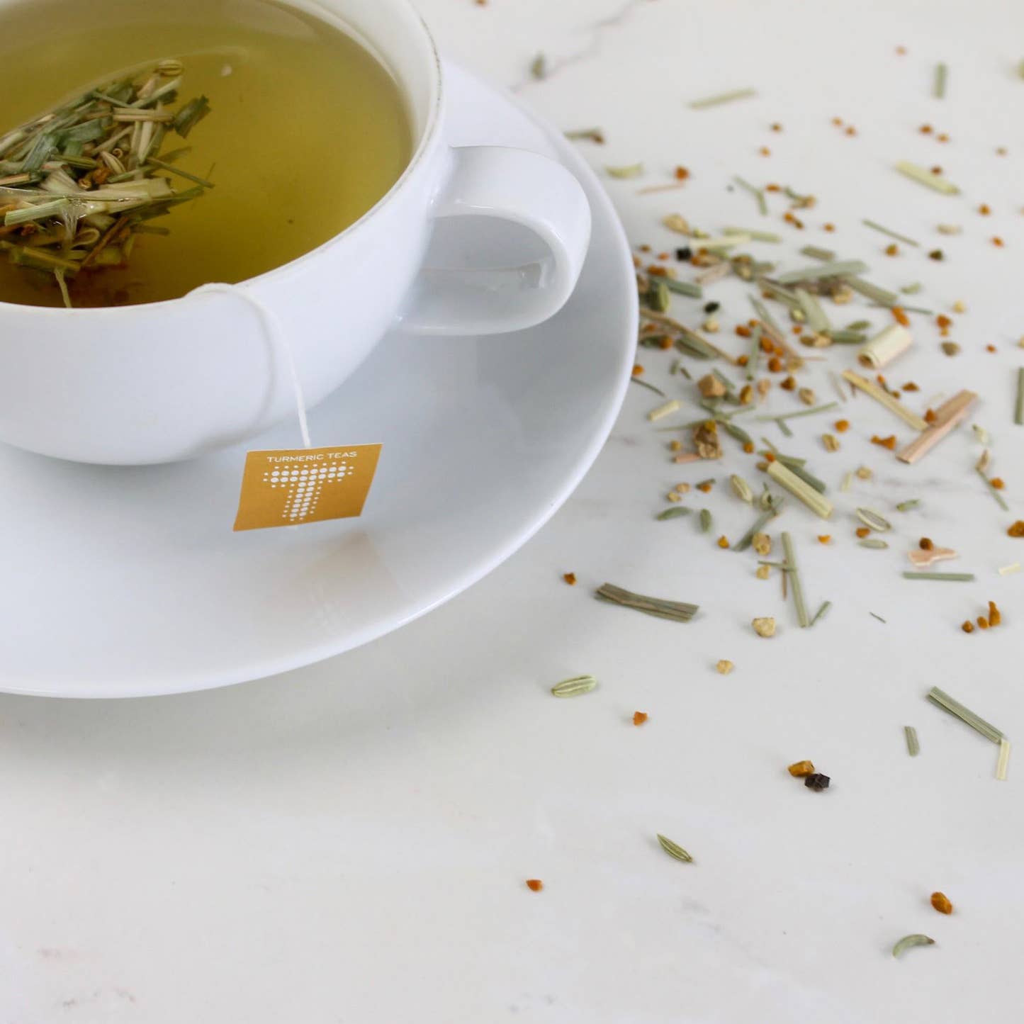 Dusk by Turmeric Teas tea sachet in a white tea cup with saucer and loose leaf tea in background